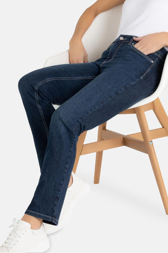 Jean bleu droit de MAC, porté avec des baskets blanches et un T-shirt blanc, assis sur une chaise blanche.