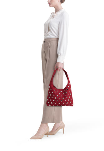 Sac à dos rouge de My Jewellery Bags, orné de studs couleur argent, porté avec une blouse blanche et un pantalon beige.