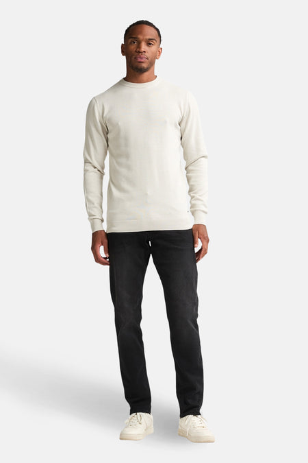 Man, staand, beige trui, zwarte jeans, witte sneakers.
