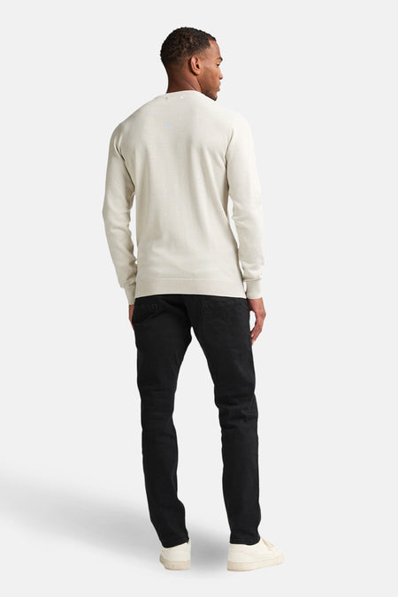 Man van achteren in een beige trui, zwarte broek en witte sneakers.