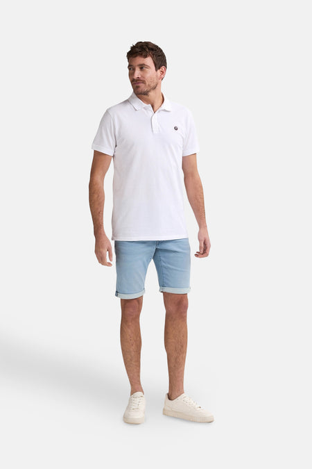 Polo blanc à manches courtes de Petrol Industries, porté avec des shorts en denim et des baskets blanches.
