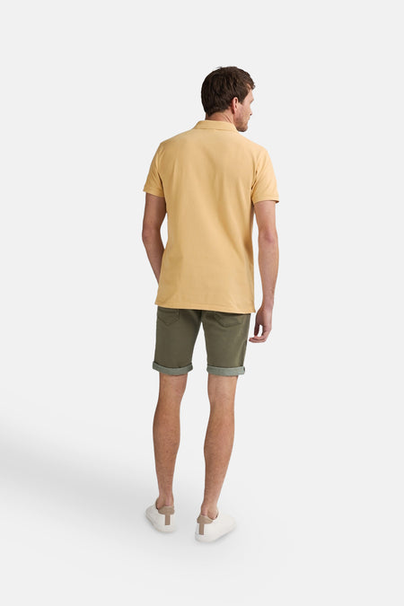 Gele polo met korte mouwen van Petrol Industries®, gezien van achteren, gecombineerd met een groene short en witte schoenen.
