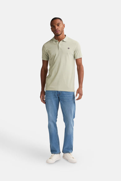 Polo vert de manches courtes de Petrol Industries®, avec un petit logo sur la poitrine, associé à des jeans bleus et des baskets blanches.
