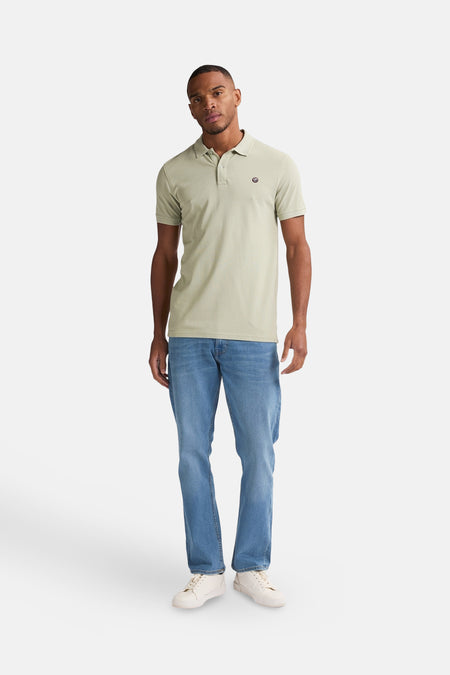 Polo vert de manches courtes de Petrol Industries®, avec un petit logo sur la poitrine, associé à des jeans bleus et des baskets blanches.