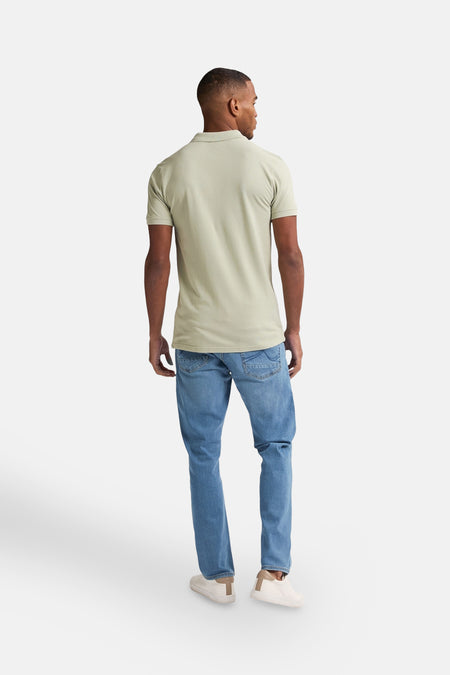 Polo vert avec manches courtes de Petrol Industries, vu de derrière, avec des jeans bleus et des baskets blanches.