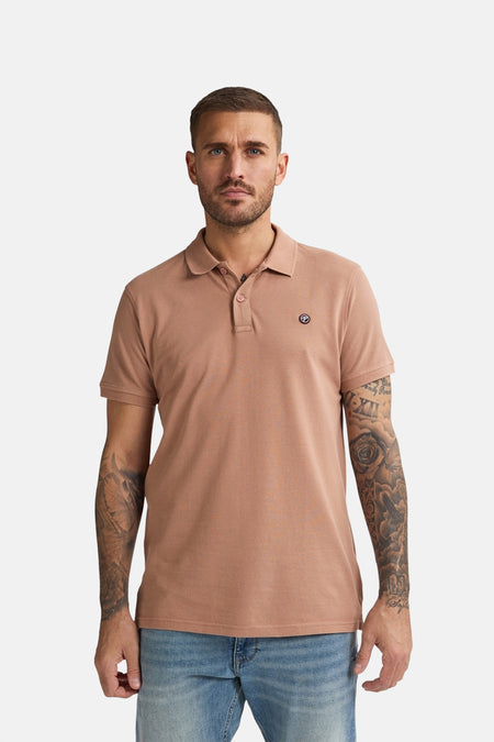Polo marron à manches courtes de Petrol Industries® avec un blblème sur la poitrine et des jeans bleu clair.