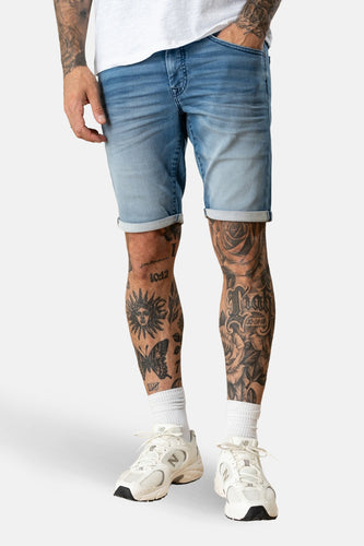 Blauwe jeansshort van Petrol Industries, met opgerolde pijpen en gedragen met witte sneakers en sokken.

