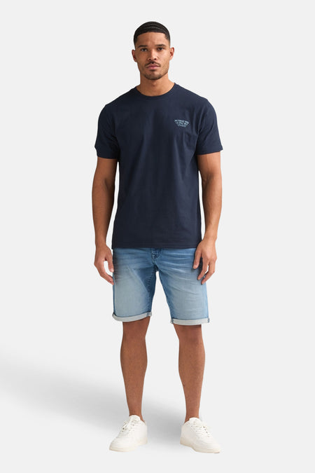 Short en jean bleu de Petrol Industries, combiné avec un t-shirt bleu foncé et des baskets blanches.