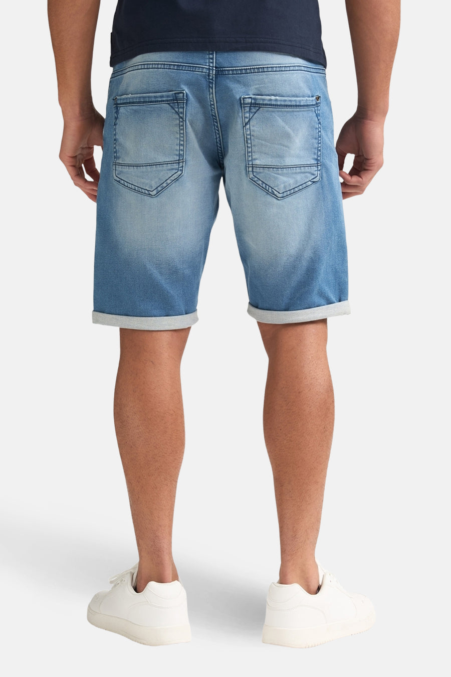 Short en jean bleu de Petrol Industries, vu de dos, avec ourlets retroussés et baskets blanches.