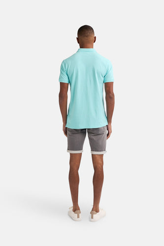 Grijze jeansshort van Petrol Industries, met omgeslagen pijpen en gedragen met een lichtblauw poloshirt.
