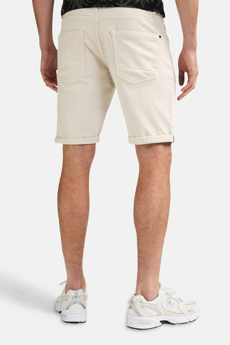 Short écru de Petrol Industries avec ourlets retroussés, porté par un homme avec des baskets blanches.