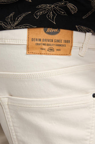 Short en jean écru de Petrol Industries®, avec étiquette de marque en cuir marron et un t-shirt noir à motif de feuilles.