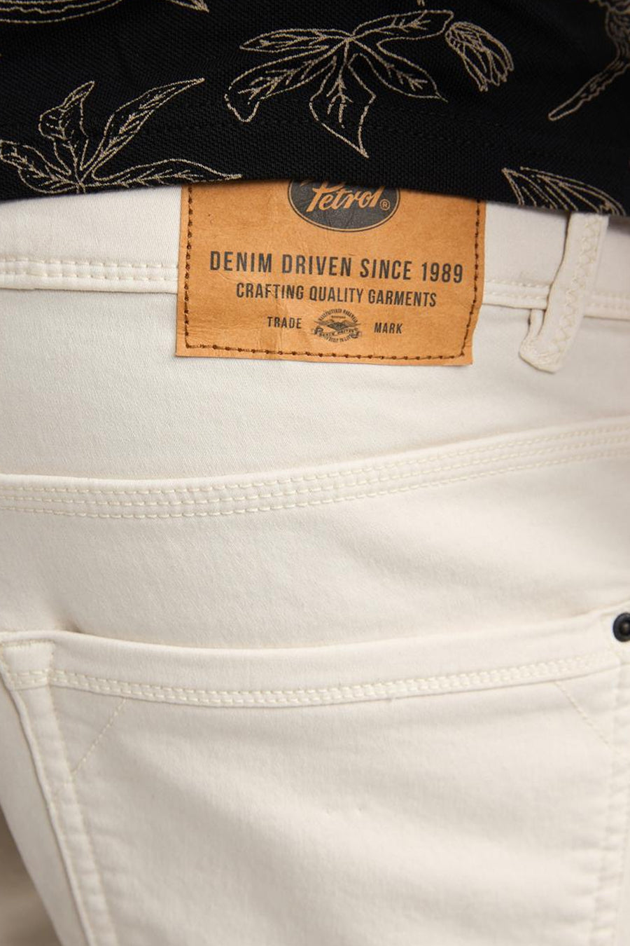 Short en jean écru de Petrol Industries®, avec étiquette de marque en cuir marron et un t-shirt noir à motif de feuilles.