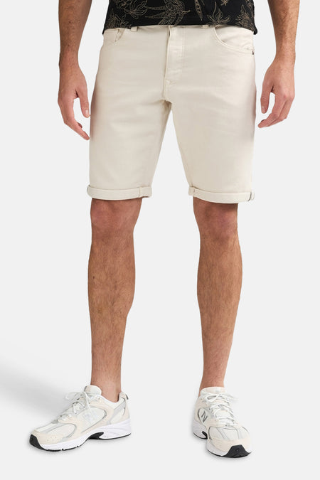 Short écru de Petrol Industries avec ourlets retroussés, porté par un homme avec une chemise foncée et des baskets blanches.