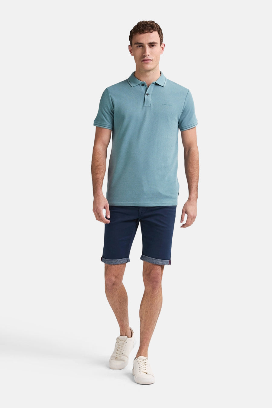 Man met blauwgroene polo, donkerblauwe shorts en witte sneakers.