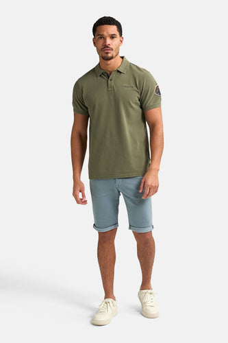 Man in kaki poloshirt, blauwe shorts en crèmekleurige schoenen.