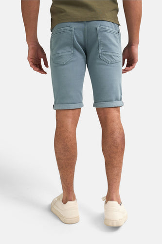 Achterkant van een man in blauw-groene shorts en crème kleurige sneakers.
