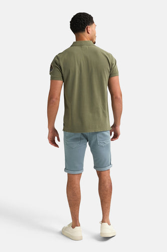 Man van achteren, groene polo, blauwe korte broek, witte sneakers.