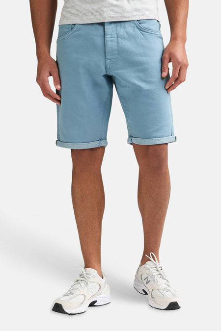 Short bleu de Petrol Industries® avec ourlets retroussés, porté par un homme avec un t-shirt gris rayé et des baskets blanches.