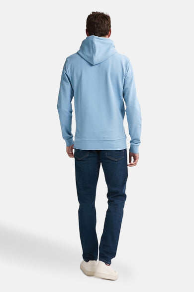 Pull-over bleu avec capuche de Petrol Industries, vu par derrière, associé à des jeans bleu marine et des chaussures écru.