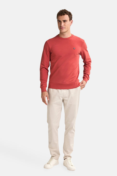 Pull-over rouge de Petrol Industries, avec des manches longues et un logo subtil sur la poitrine, associé à un pantalon beige et des chaussures.