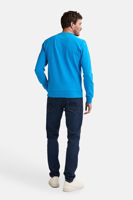 Blauwe sweater met ronde hals van Petrol Industries, gezien van achteren, gecombineerd met donkere jeans en lichte sneakers.