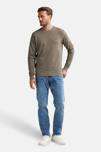 Kaki sweater van Petrol Industries, met lange mouwen, gecombineerd met een blauwe jeans en witte sneakers.