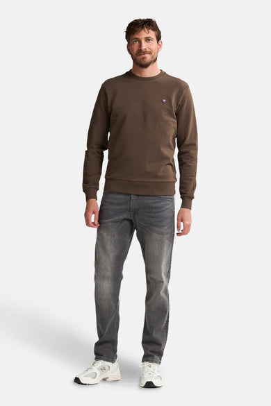 Pull-over marron de Petrol Industries avec un col rond, associé à des jeans gris et des baskets blanches.