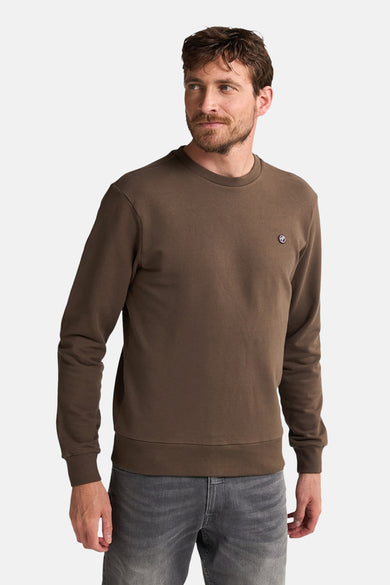 Gilet marron de Petrol Industries® avec col rond et petit logo sur la poitrine, associé à des jeans gris.