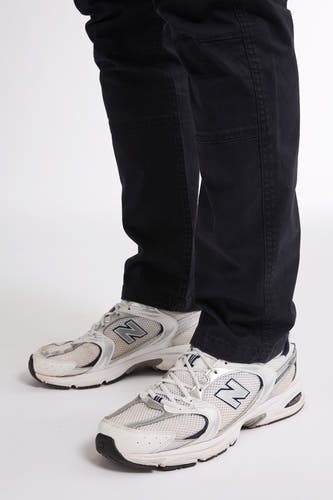 Pantalon de travail noir de Petrol Industries, avec des poches cousues et porté avec des baskets blanches.