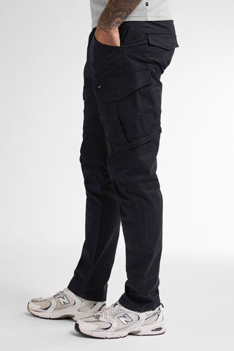 Pantalon cargo noir de Petrol Industries, avec des poches et porté avec des baskets blanches.