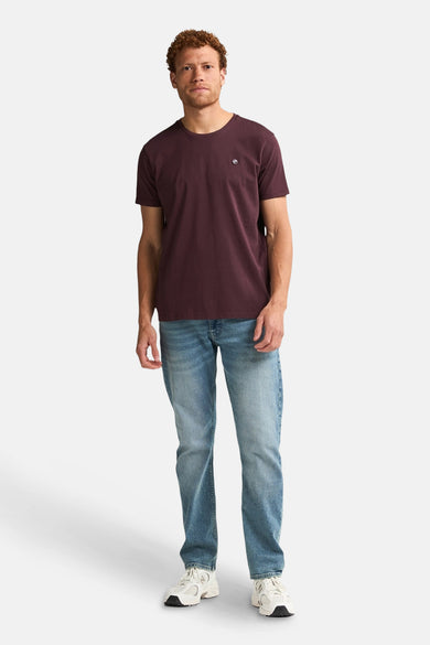T-shirt Bordeaux à manches courtes de Petrol Industries, porté avec des jeans et des baskets blanches.