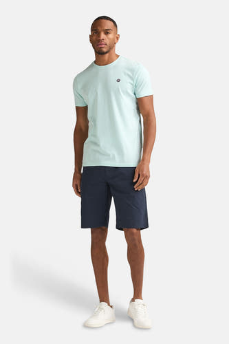 T-shirt vert à manches courtes de Petrol Industries, avec un petit logo et combiné avec un short bleu foncé et des baskets blanches.
