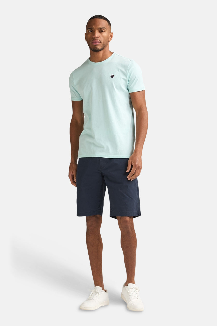 T-shirt vert à manches courtes de Petrol Industries, avec un petit logo et combiné avec un short bleu foncé et des baskets blanches.
