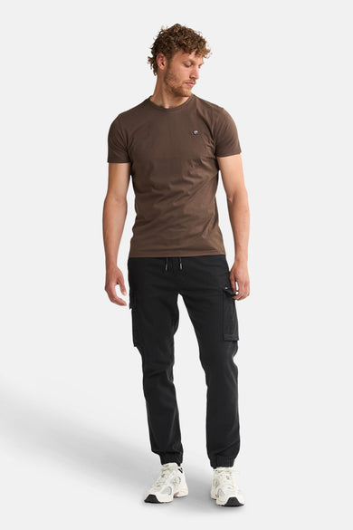 T-shirt marron à manches courtes de Petrol Industries, avec un petit logo sur la poitrine et porté avec un pantalon cargo noir.
