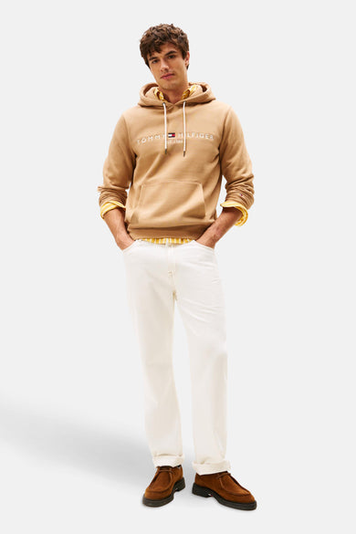 Gilet beige à capuche de Tommy Hilfiger, avec des manches longues et un pantalon blanc et des chaussures marron.