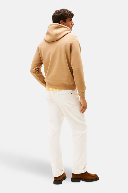 Pull-over beige avec col rond de TOMMY HILFIGER, avec un t-shirt rayé visible en dessous, porté avec des pantalons blancs et des chaussures marron, vue arrière.