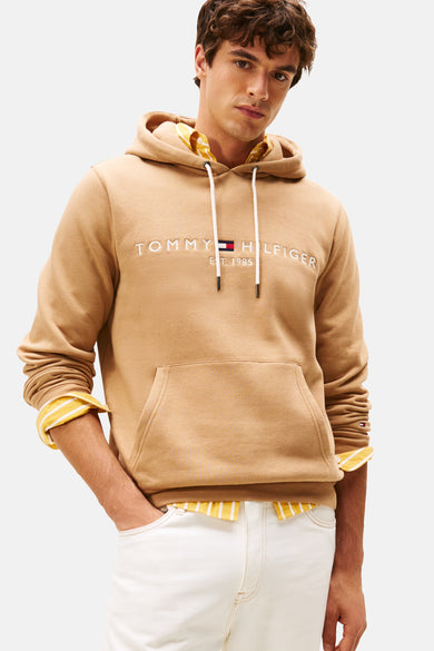 Gilet beige avec col rond de Tommy Hilfiger, porté sur une chemise rayée et des pantalons blancs.