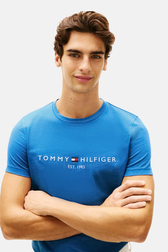 T-shirt bleu à manches courtes de Tommy Hilfiger, porté par un homme avec les bras croisés.
