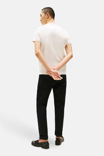 T-shirt beige à manches courtes de TOMMY HILFIGER, vu de l'arrière, associé à des jeans noirs et des loafers.