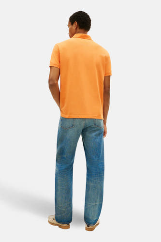 Polo orange à manches courtes de Tommy Hilfiger, vue de dos, avec un jean bleu et des chaussures crème.
