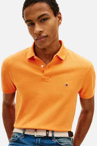 Polo orange à manches courtes de Tommy Hilfiger, avec un logo brodé et portée avec un jean et une ceinture.
