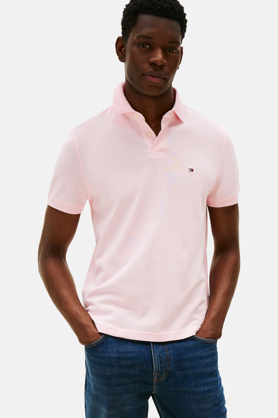 Polo rose à manches courtes de TOMMY HILFIGER, vu de derrière, associé à des jeans bleus marine et des loafers marrons.