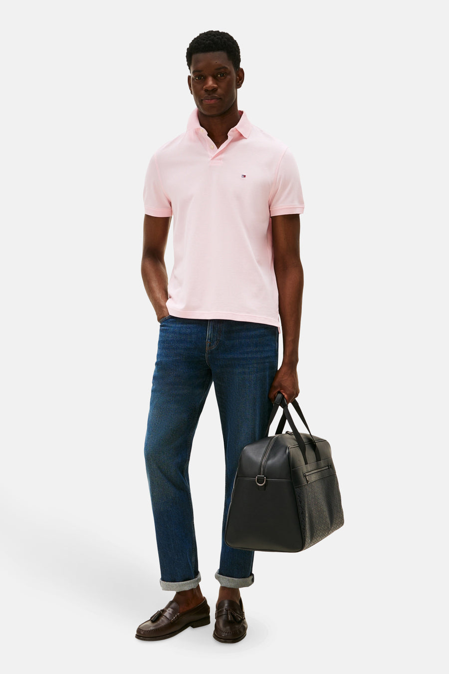 Polo rose à manches courtes de TOMMY HILFIGER, associé à des jeans foncés, des loafers en cuir et une pochette noire.