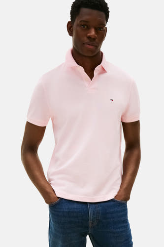 Polo rose à manches courtes de TOMMY HILFIGER, porté avec des jeans bleus, les mains dans les poches.