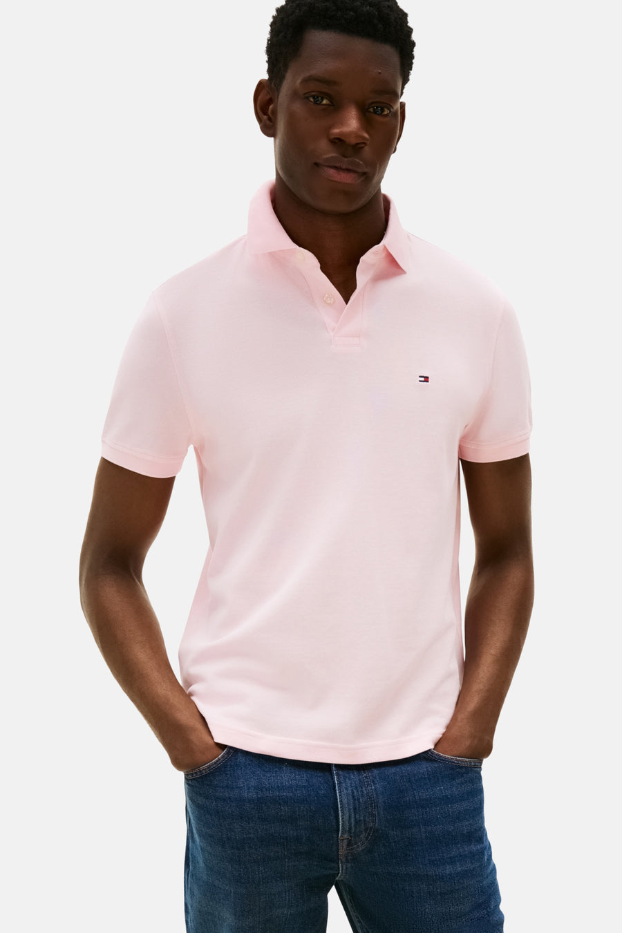 Polo rose à manches courtes de TOMMY HILFIGER, porté avec des jeans bleus, les mains dans les poches.
