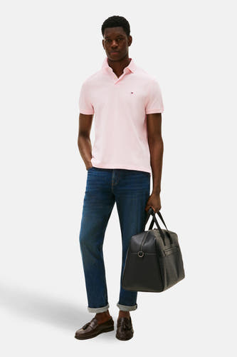 Polo rose à manches courtes de TOMMY HILFIGER, porté avec des jeans et des mocassins en cuir, avec une valise noire.
