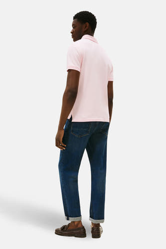 Polo rose à manches courtes de TOMMY HILFIGER, avec un col classique et porté avec des jeans foncés et des loafers marrons.