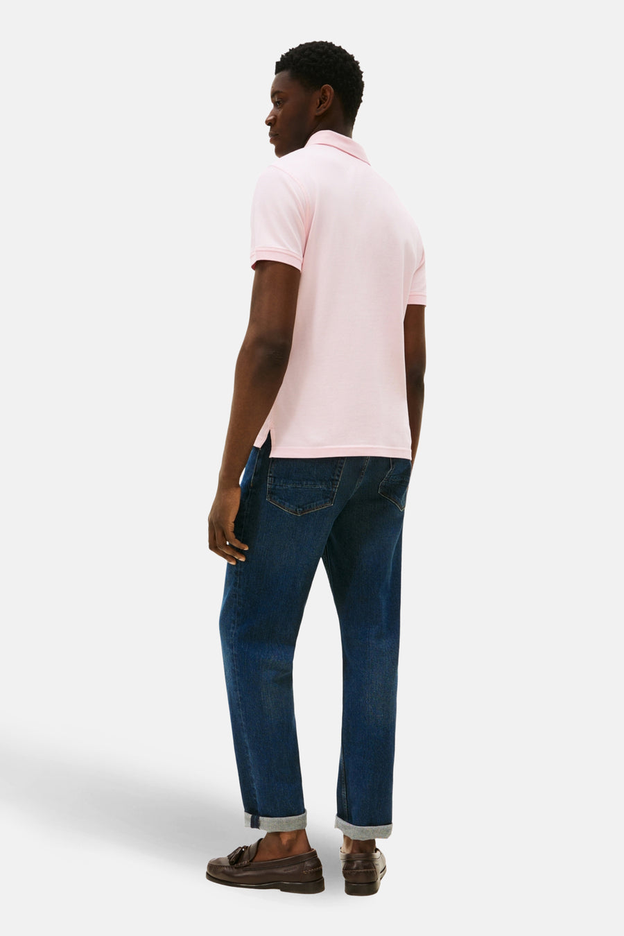 Polo rose à manches courtes de TOMMY HILFIGER, avec un col classique et porté avec des jeans foncés et des loafers marrons.