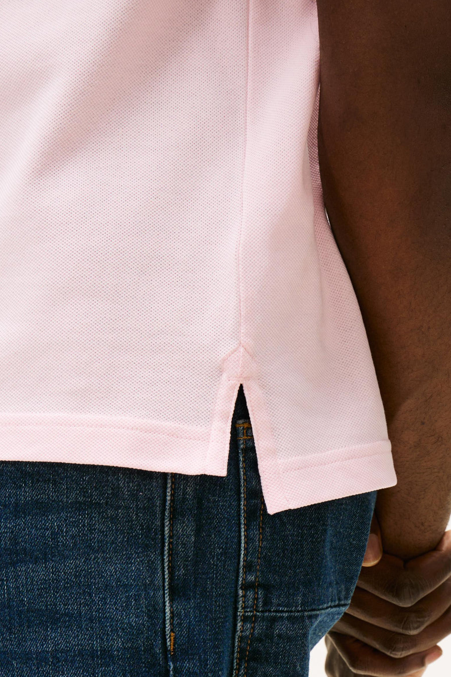 Polo rose à manches courtes de TOMMY HILFIGER, en tissu piqué et avec une fente latérale, porté avec un short en denim foncé.